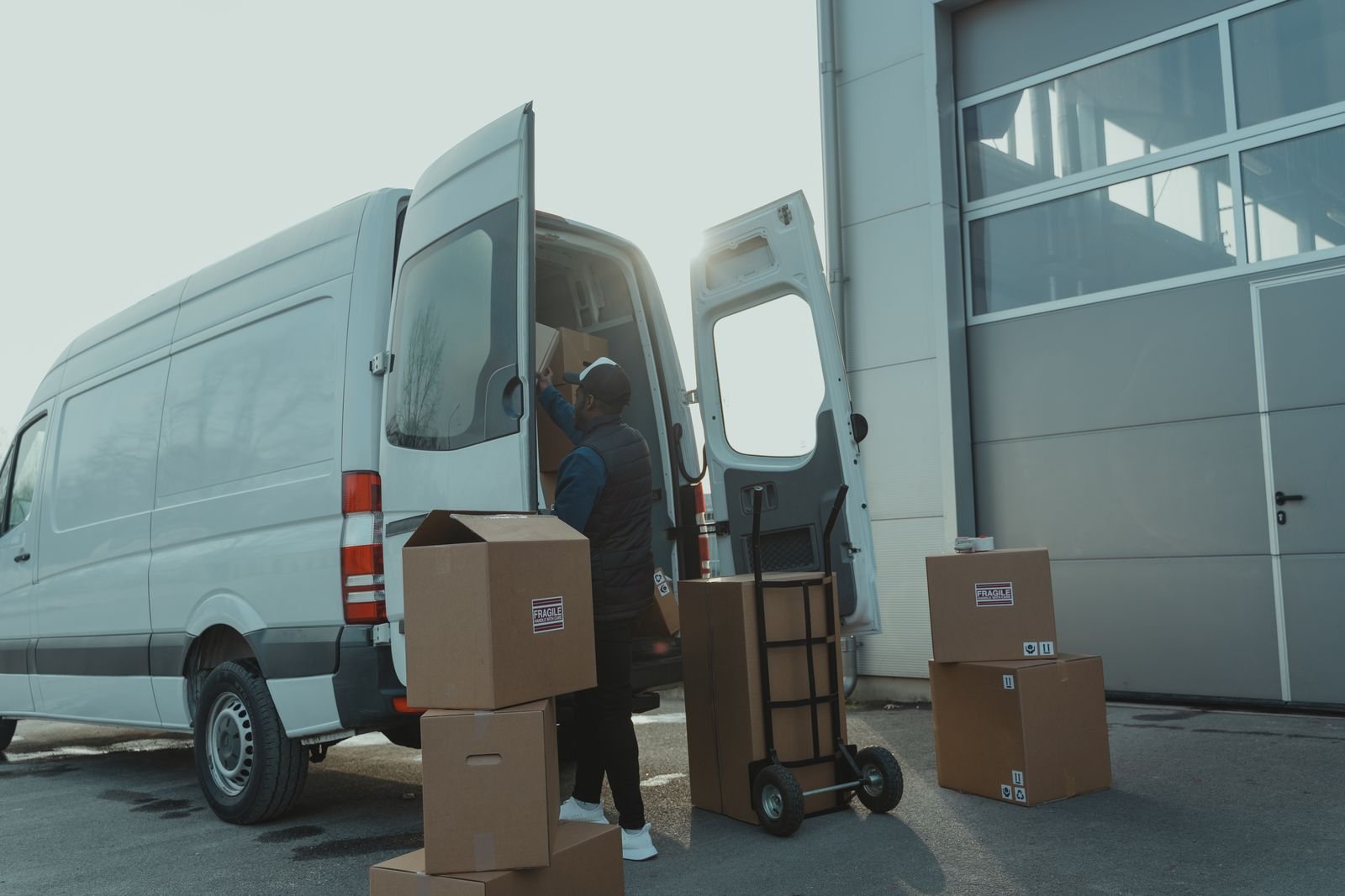 Un repartidor carga cajas en una camioneta, junto a un carrito con más paquetes